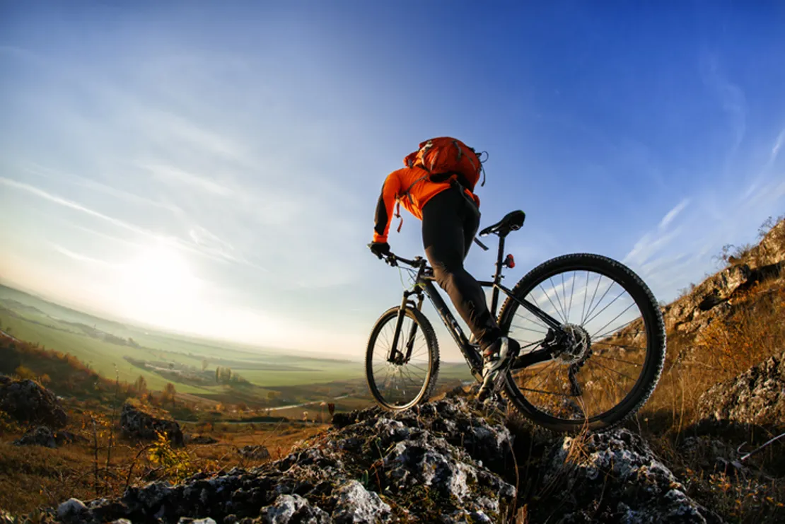 Rear View Of A Man On A Mountain Bike Riding Through The Mountains With A Red Backpack