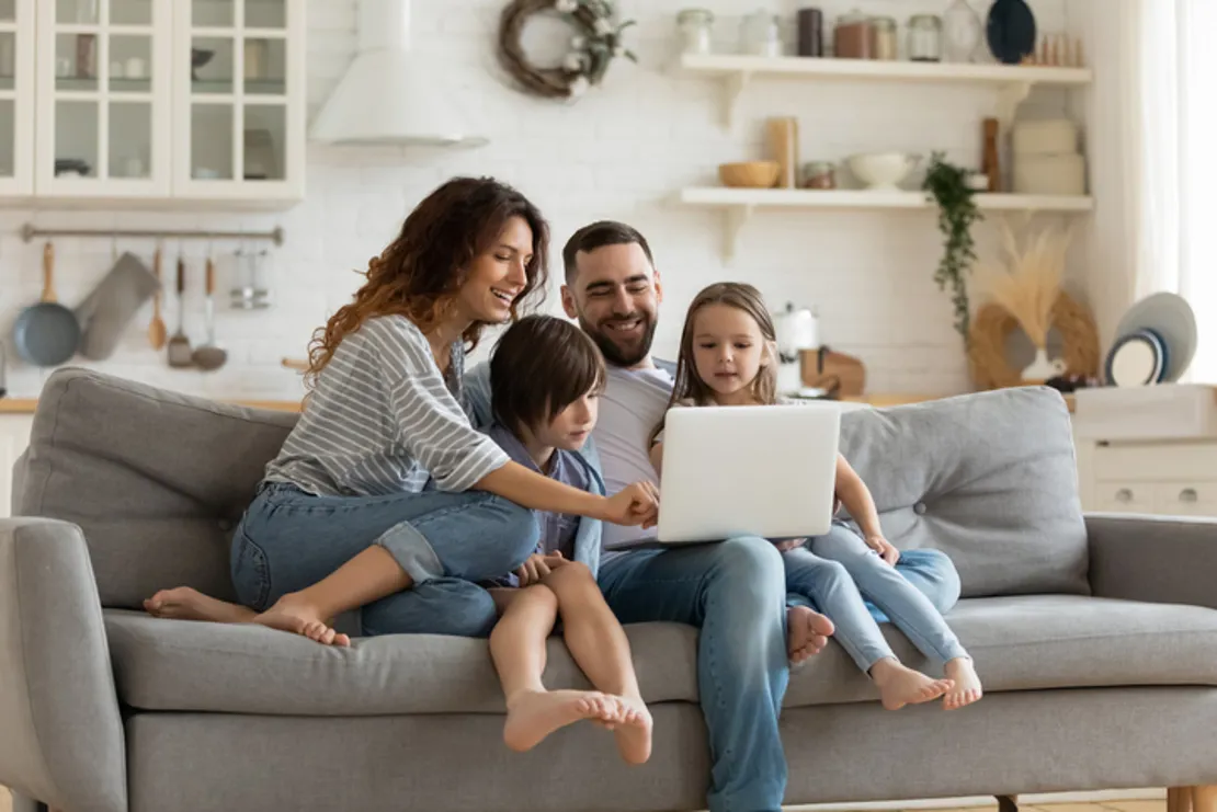 Happy Couple Family With Small Children Sitting On Sofa Using A Laptop Together