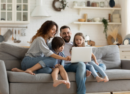 Happy Couple Family With Small Children Sitting On Sofa Using A Laptop Together