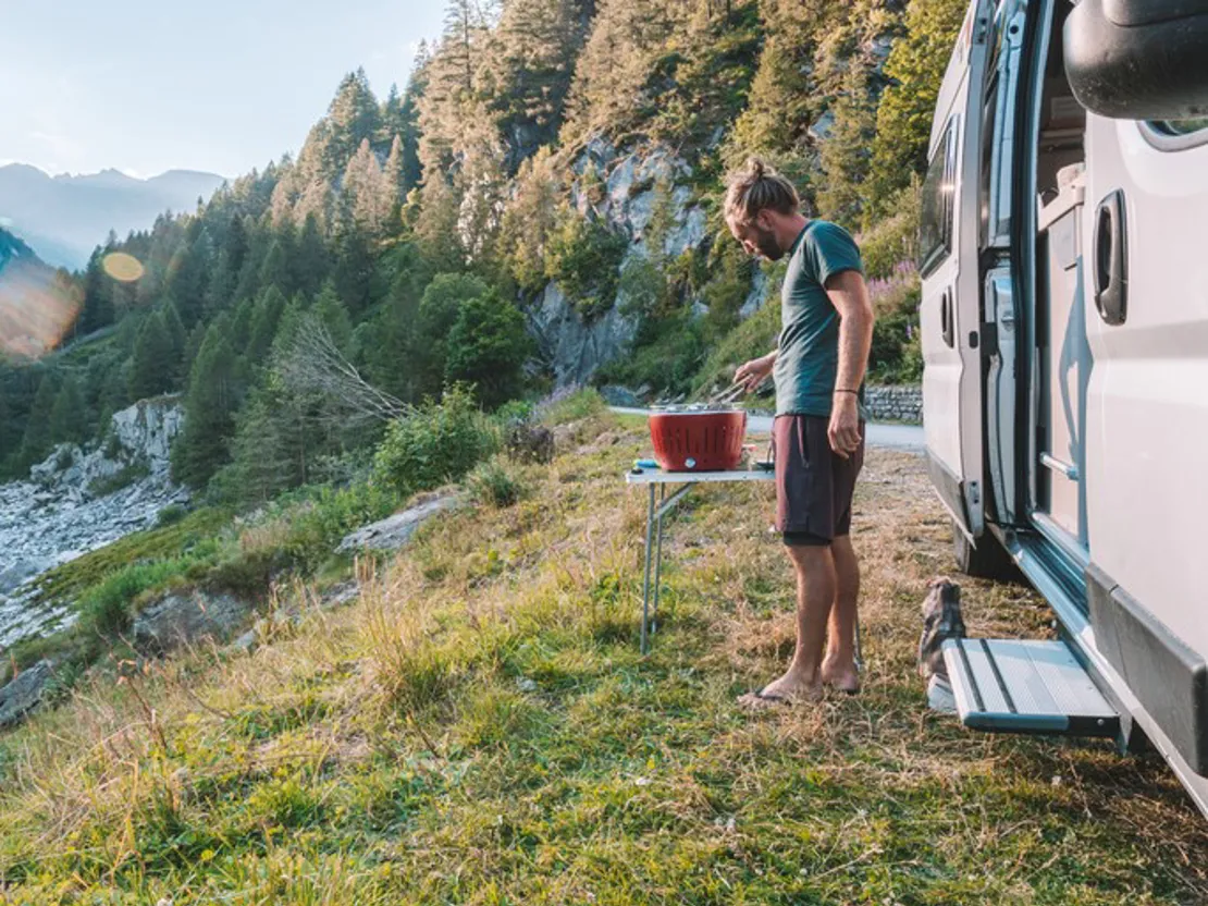 Man BBQing outside his caravan on a mountain side